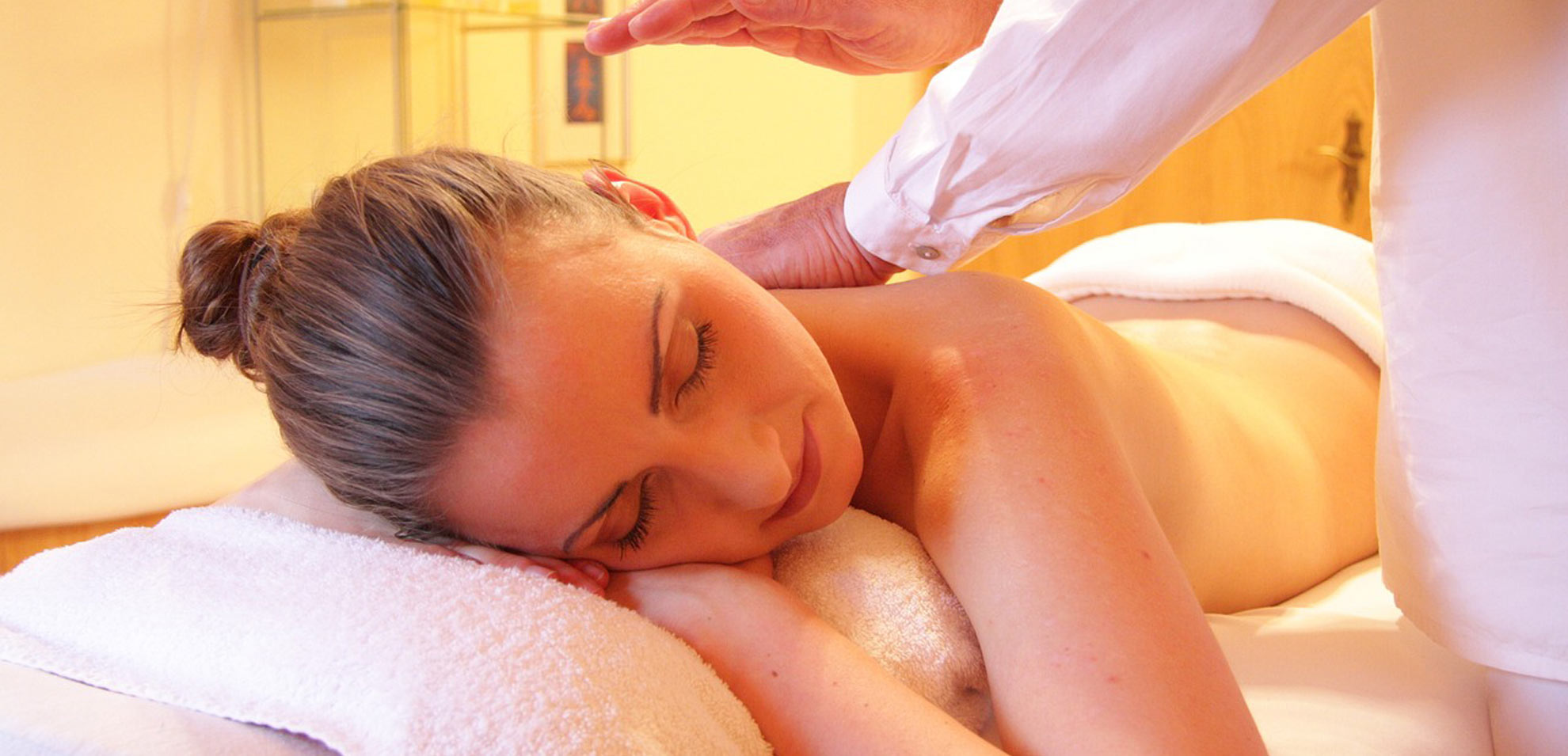 Frau mit geschlossenen Augen bei Gesichtsmassage, eingerollt in weißes Handtuch, entspannte Atmosphäre.