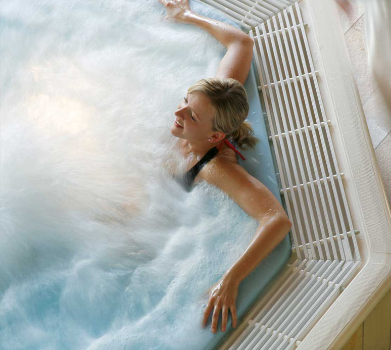 Frau im Whirlpool mit Schaumkragen im Nackenbereich, helles Tageslicht fällt auf das Wasser.