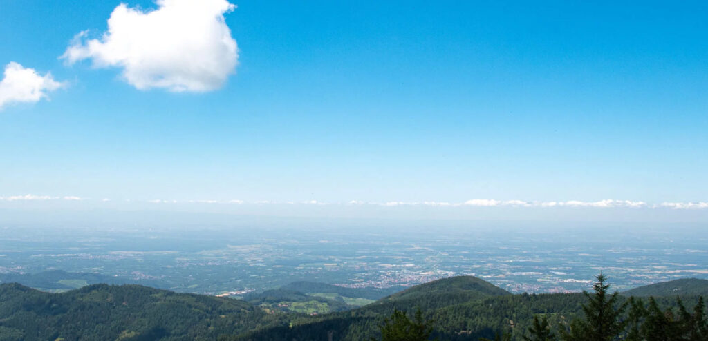 Panoramablick über hügelige Landschaft mit bewaldeten Höhenzügen unter blauem Himmel.