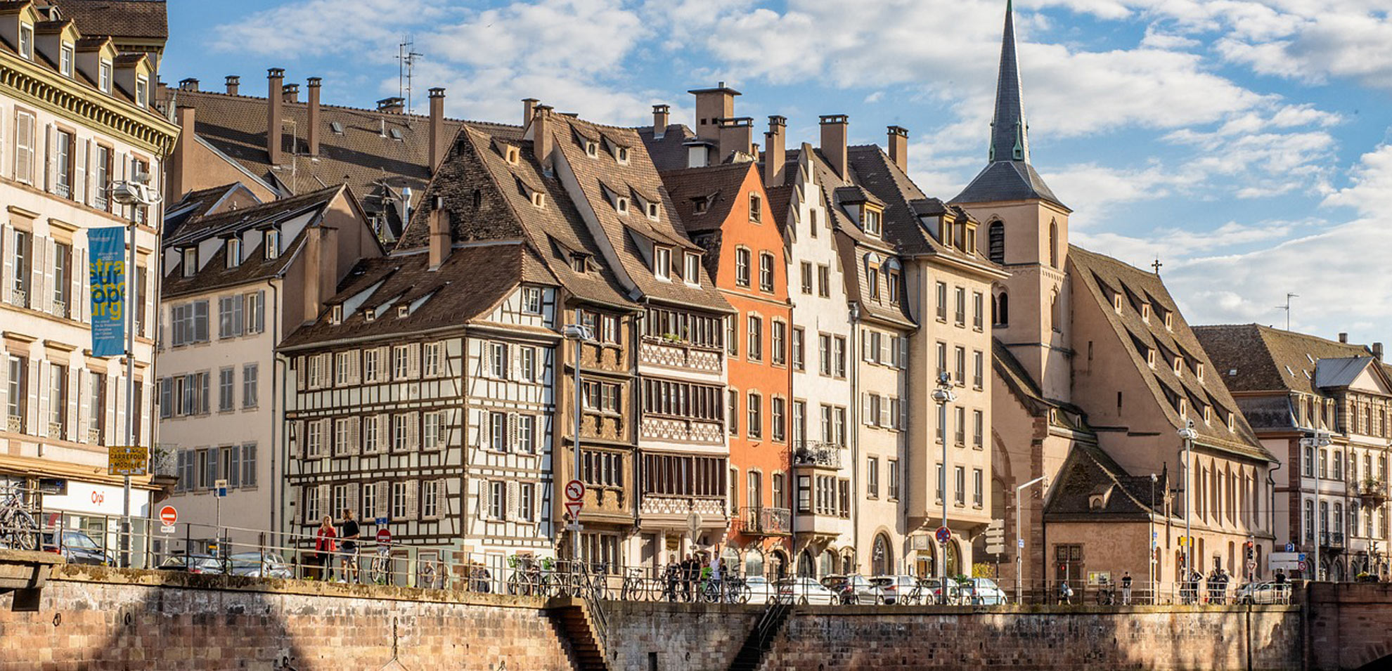 Blick auf Fachwerkhäuser am Flussufer in Straßburg, spiegelndes Wasser im Vordergrund.
