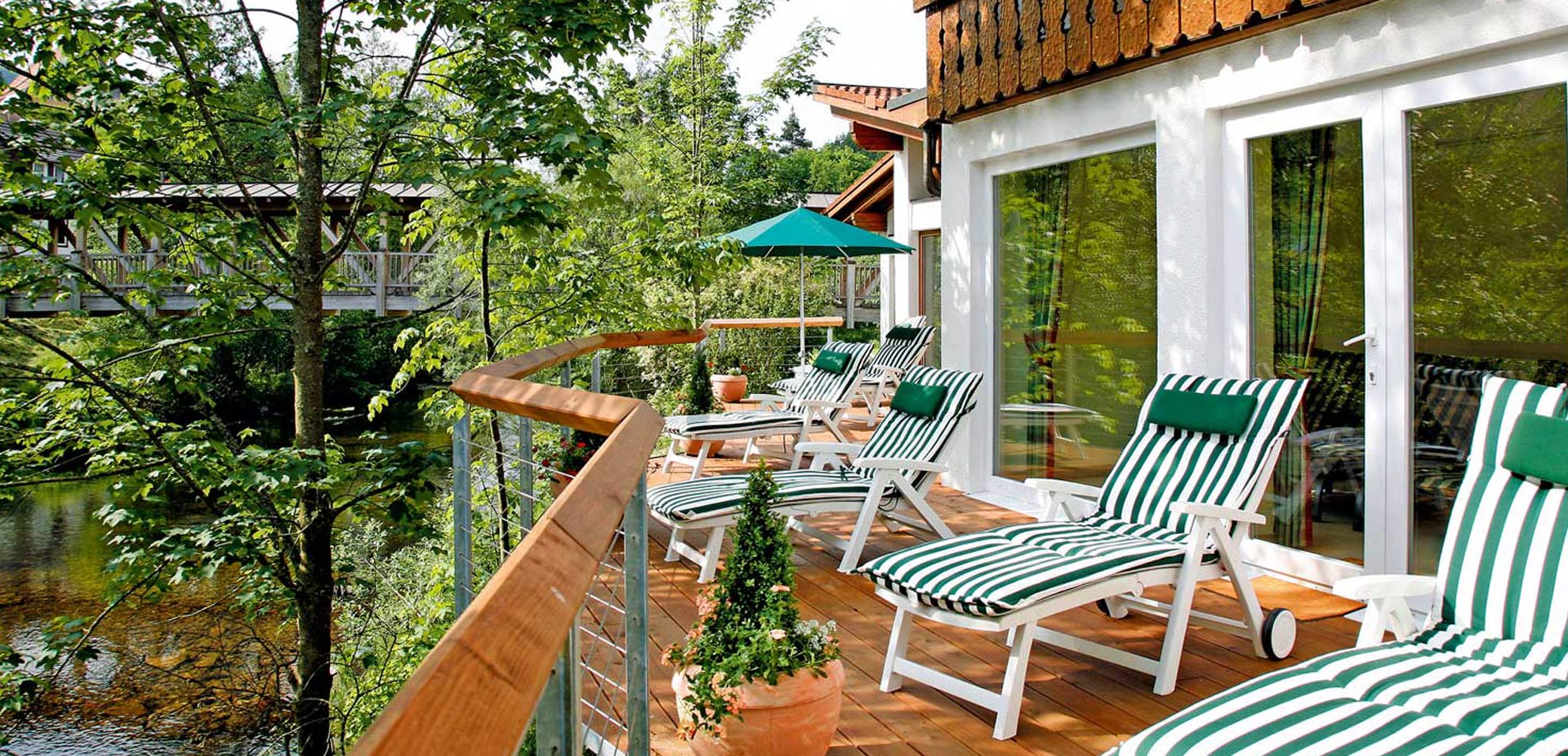 Balkon mit weißer Sitzgruppe und rundem Tisch, Blick auf umliegende Natur, rote Markise leicht eingefahren.
