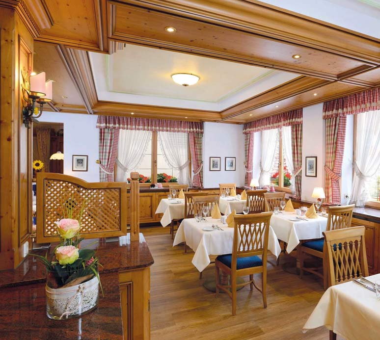 Speisesaal mit gedeckten Tischen, Holzdecke, Kronleuchter und Ausblick ins Freie.