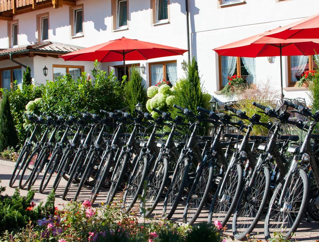 Fahrradverleih des Hotels mit mehreren aufgereihten Cityrädern, rotes Sonnendach und weiße Fassade im Hintergrund.