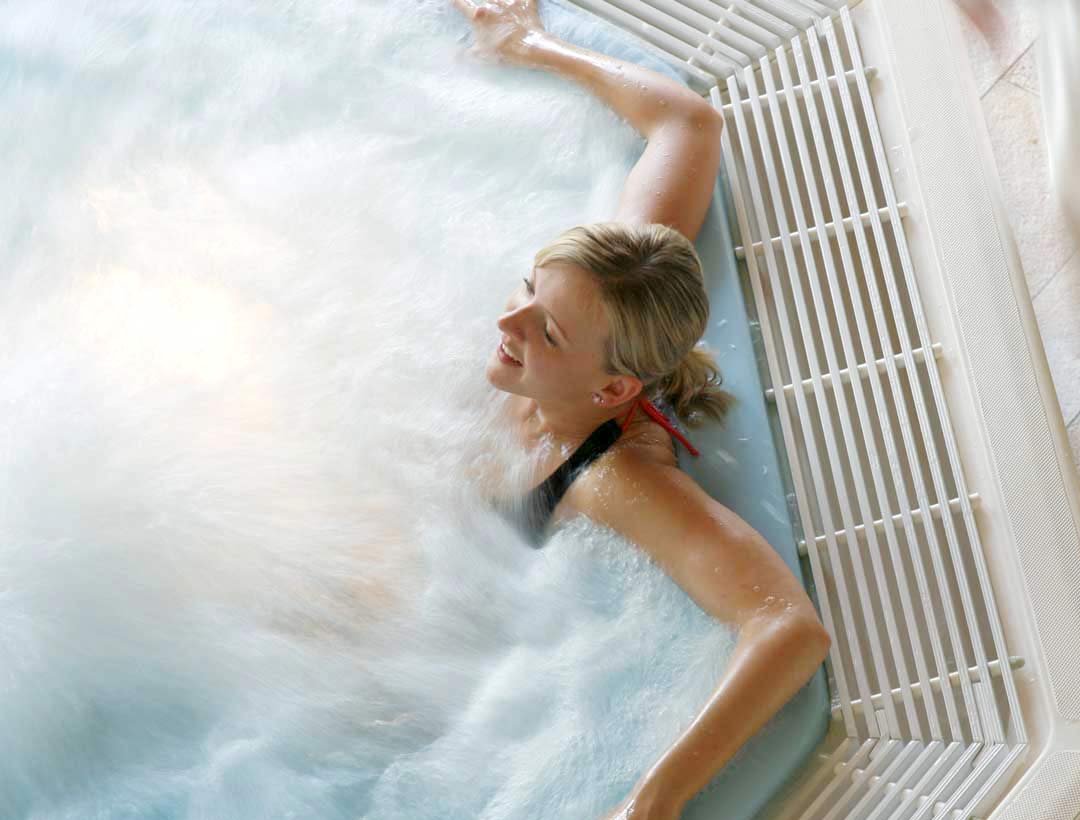 Frau entspannt im sprudelnden Whirlpool, halbseitiges Profil mit zurückgelehntem Kopf, umgeben von weißem Wasserdampf.