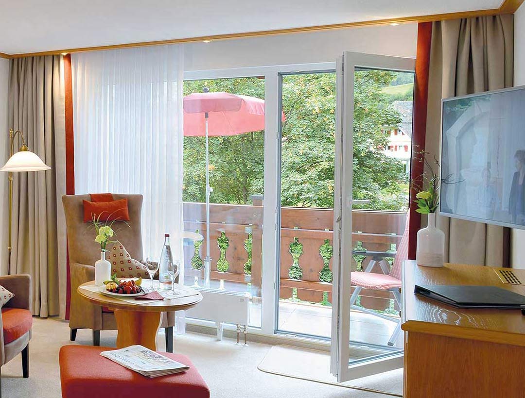 Doppelbett-Zimmer mit roten Vorhängen, Holzmöbeln und Fenster mit Ausblick, dekoratives Bild an der Wand.