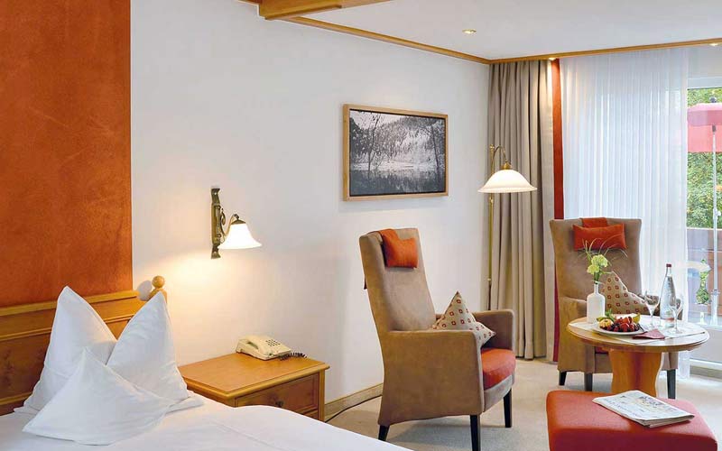 Doppelbett-Zimmer mit roten Vorhängen, Holzmöbeln und Fenster mit Ausblick, dekoratives Bild an der Wand.