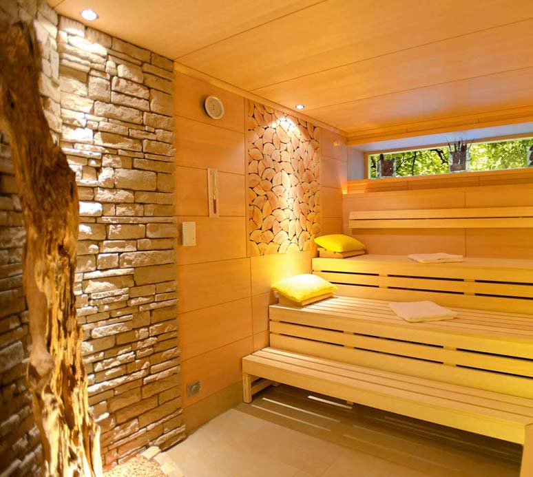Innenaufnahme einer Sauna mit Holzliegen, Rückwand aus Naturstein und sanfter Beleuchtung.