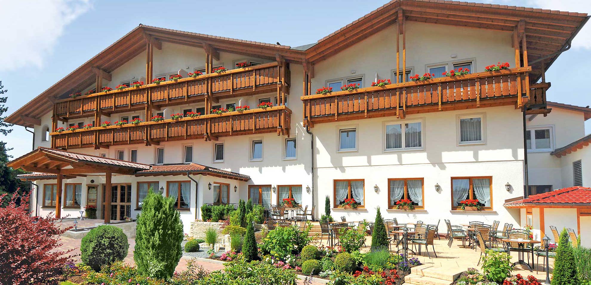 Außenansicht des Hotels mit Balkonen, weißen Sonnenschirmen und blühenden Sträuchern.