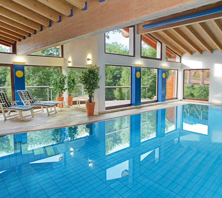 Großer Innenpool mit türkisfarbenem Wasser, breiten Fenstern und Holzdecke.