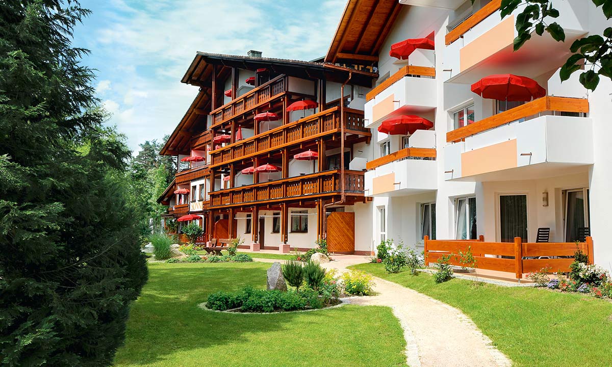 Hotelrückseite mit üppigem Garten, Balkonen mit Blumenschmuck und gepflegtem Rasen.