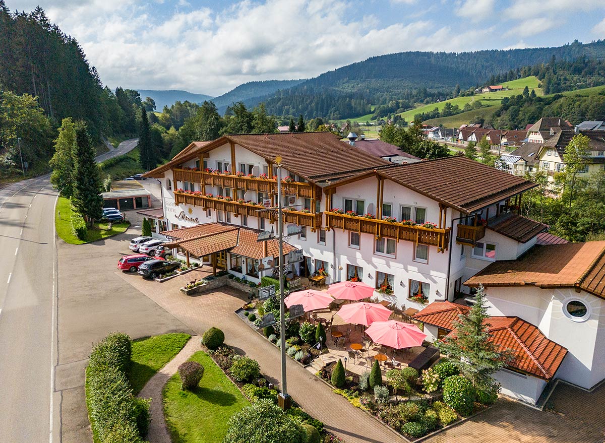 Luftaufnahme des Hotels mit braunem Dach, rosa Sonnenschirmen auf der Terrasse und Parkflächen.