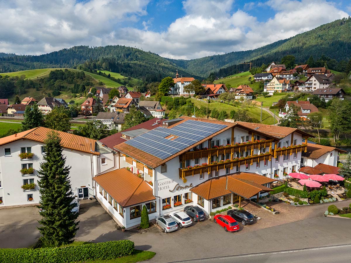 Außenansicht mit begrüntem Parkplatz, Hotelkomplex mit Holzelementen und Balkonen.