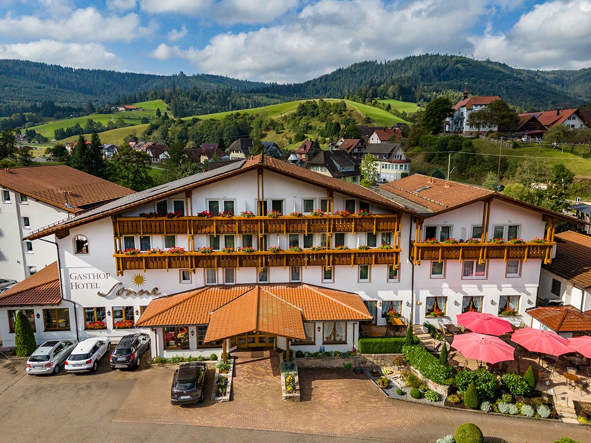Frontsicht auf Hoteltrakt mit langem Flachdach, Nebengebäude und Einfahrt, eingebettet in grüne Hügellandschaft.