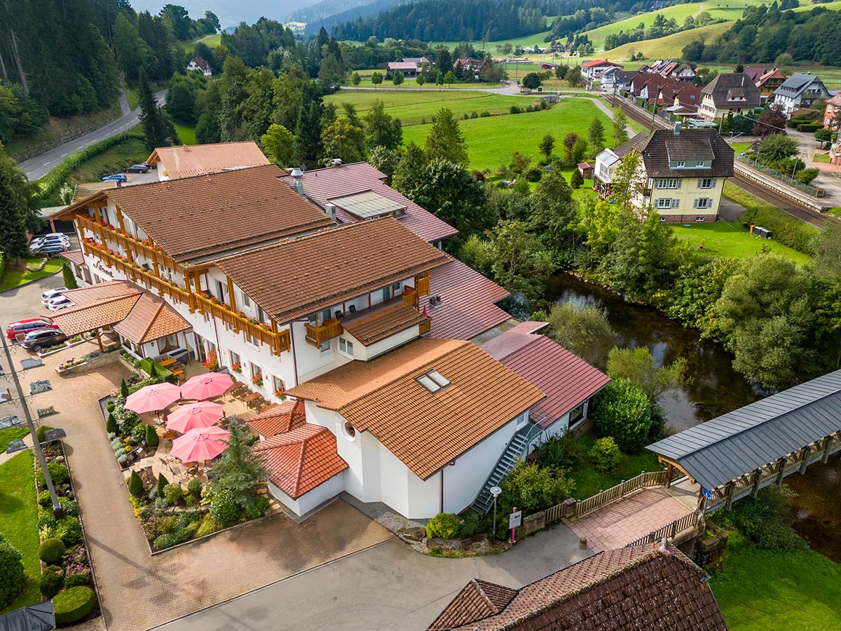 Vogelperspektive auf Hotel mit Zufahrt, mehreren Gebäudeteilen und umgebender Wiesenlandschaft.