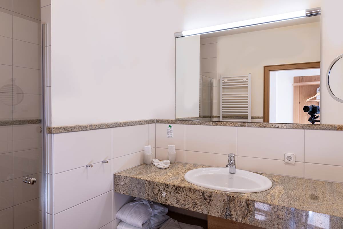 Weiß gefliestes Badezimmer mit Waschbecken, Handtuchhalter und integrierter Beleuchtung.