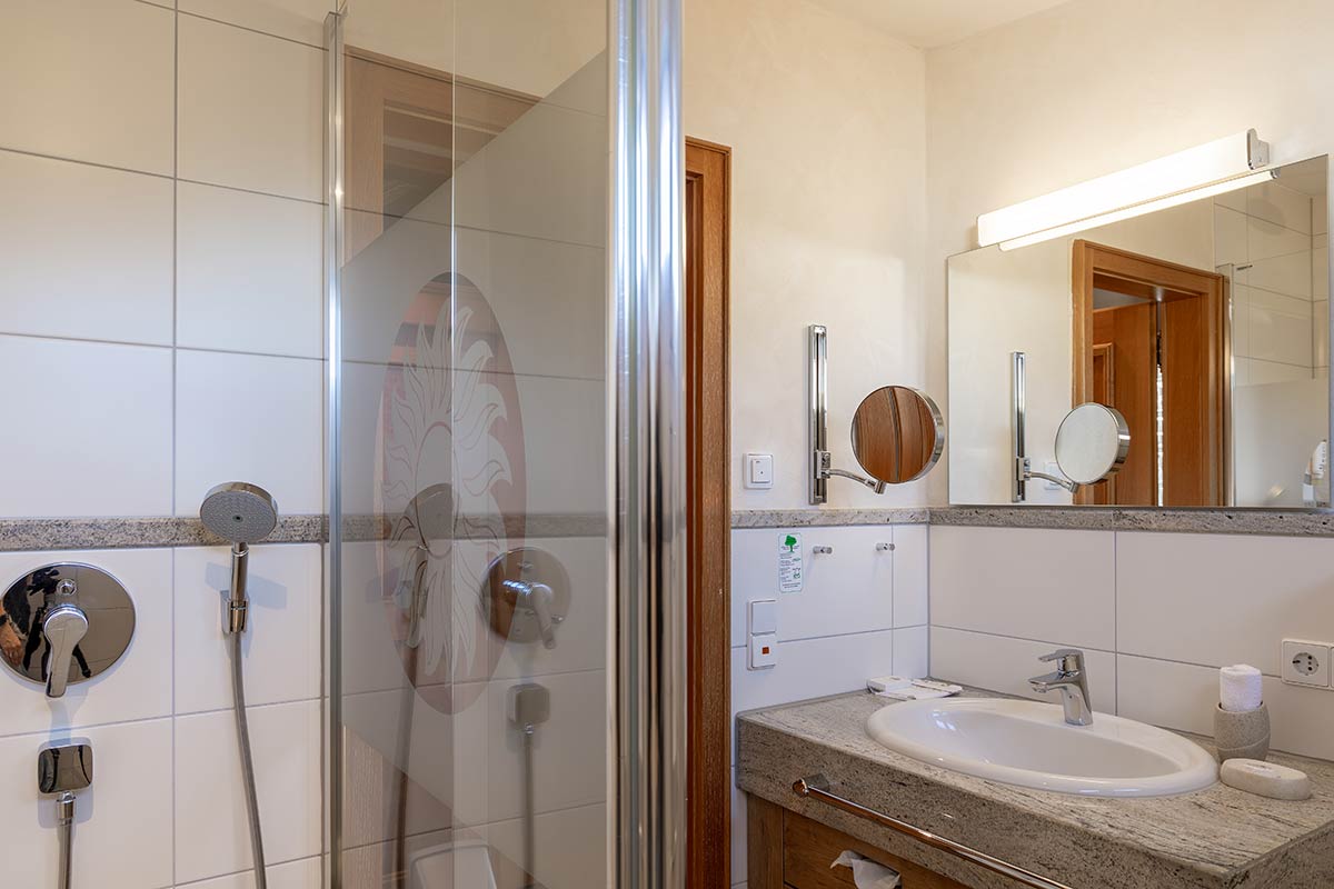 Modernes Bad mit Dusche, Glasabtrennung, Waschbecken, WC und beleuchtetem Spiegel.