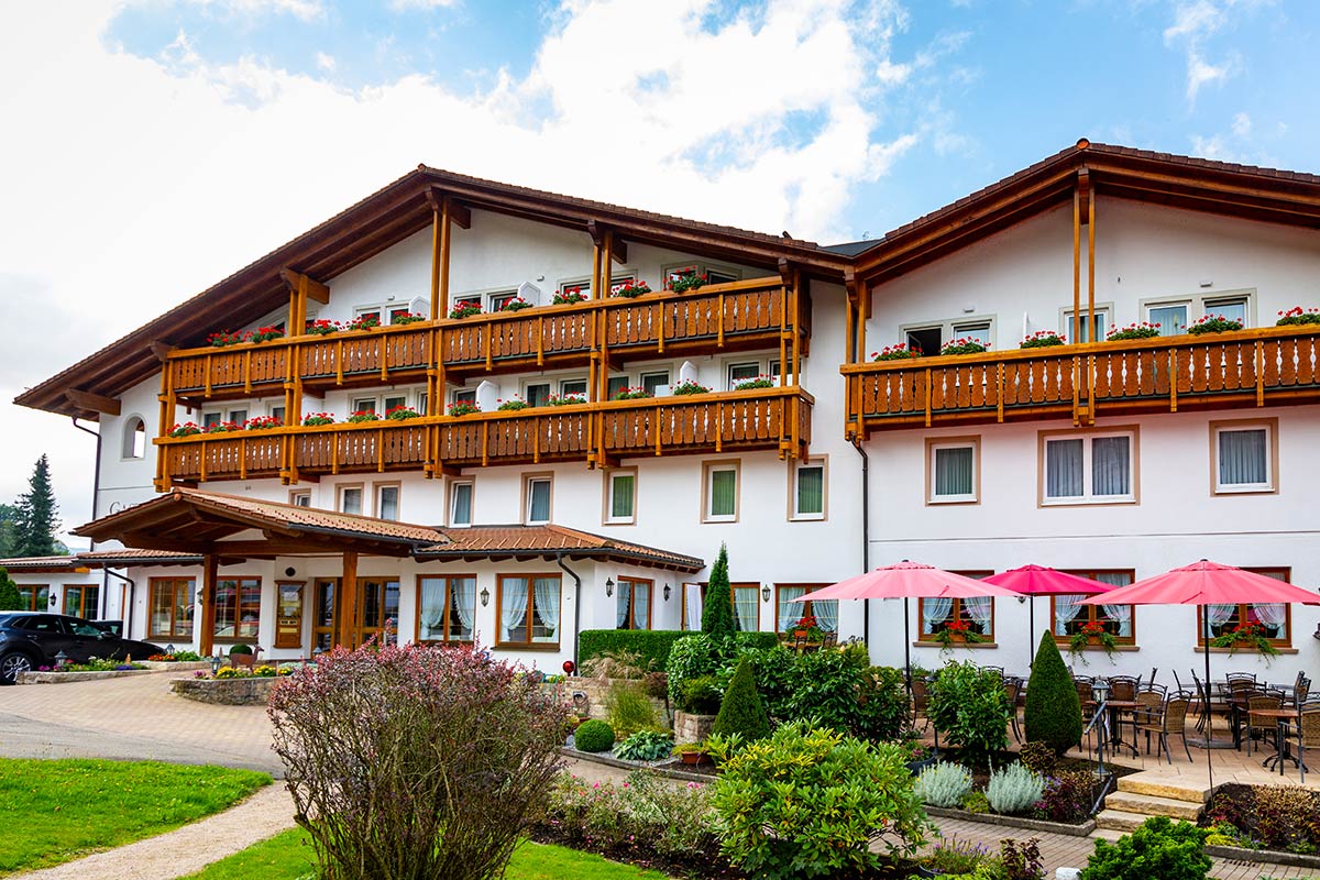 Dreistöckiges Hotel mit Holzbalkonen, Fassadenbegrünung, Garten mit Büschen und Sitzmöglichkeiten.
