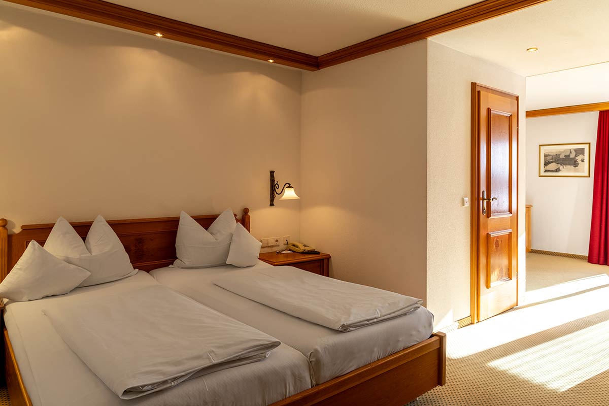 Schlafzimmer mit Doppelbett, weißer Bettwäsche, Holzmöbeln, großem Fenster und sanfter Beleuchtung.