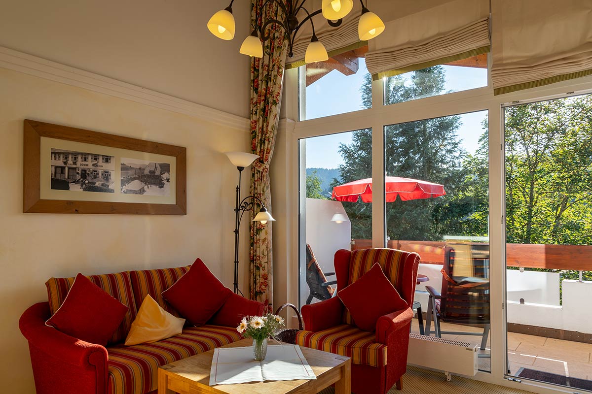 Wohnbereich mit gepolsterten Sofas in Rot, Couchtisch und Fenster mit geöffnetem Vorhang.