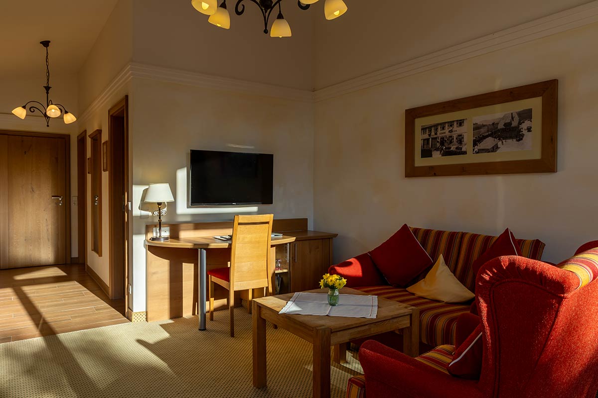 Wohnbereich mit gepolsterten Sofas in Rot, Couchtisch und Fenster mit geöffnetem Vorhang.