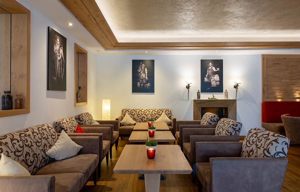 Mehrere Sofas in Grau und Beige um Couchtische gruppiert, Holzdecke mit Spotlights, Wände mit Gemälden.