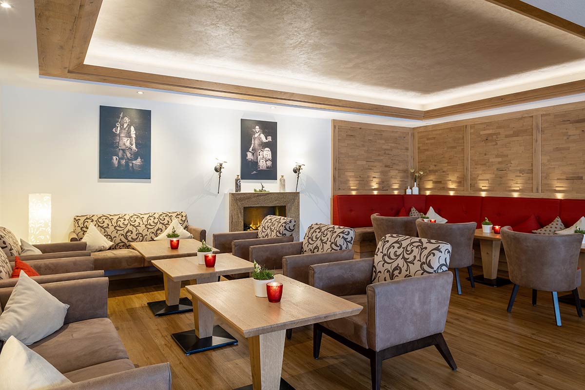 Mehrere Sofas in Grau und Beige um Couchtische gruppiert, Holzdecke mit Spotlights, Wände mit Gemälden.