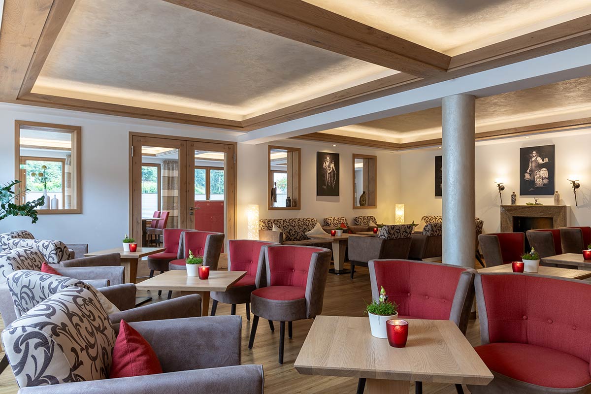 Aufenthaltsraum mit mehreren Polstermöbeln, niedrigen Tischen und geöffneten Türen zur Terrasse.