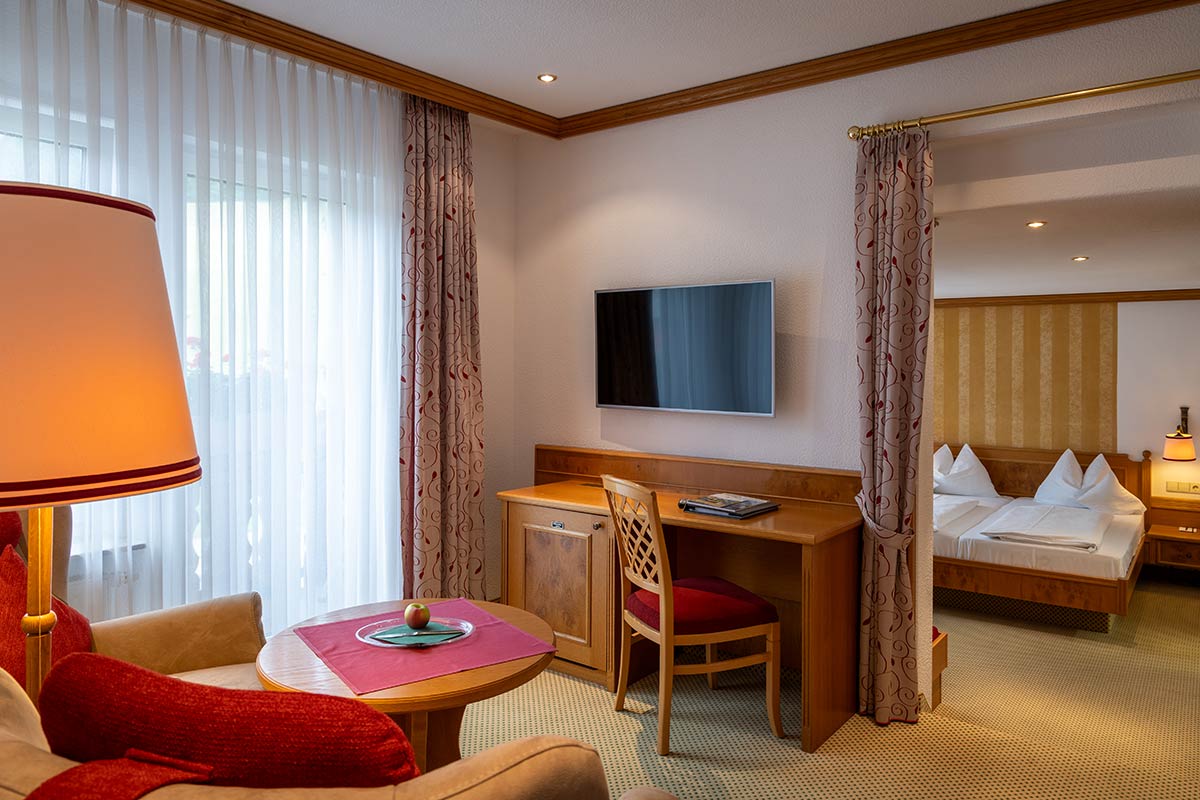 Kleiner Arbeitsbereich mit Schreibtisch, Stuhl, Fernseher auf Holzkommode, Vorhang halb geöffnet.