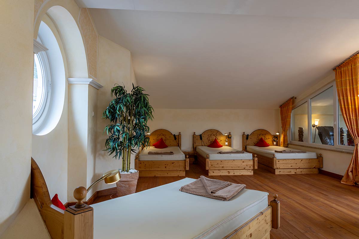 Ruhebereich mit vier gepolsterten Wellnessliegen, große Pflanze im Hintergrund, Tageslicht von links.