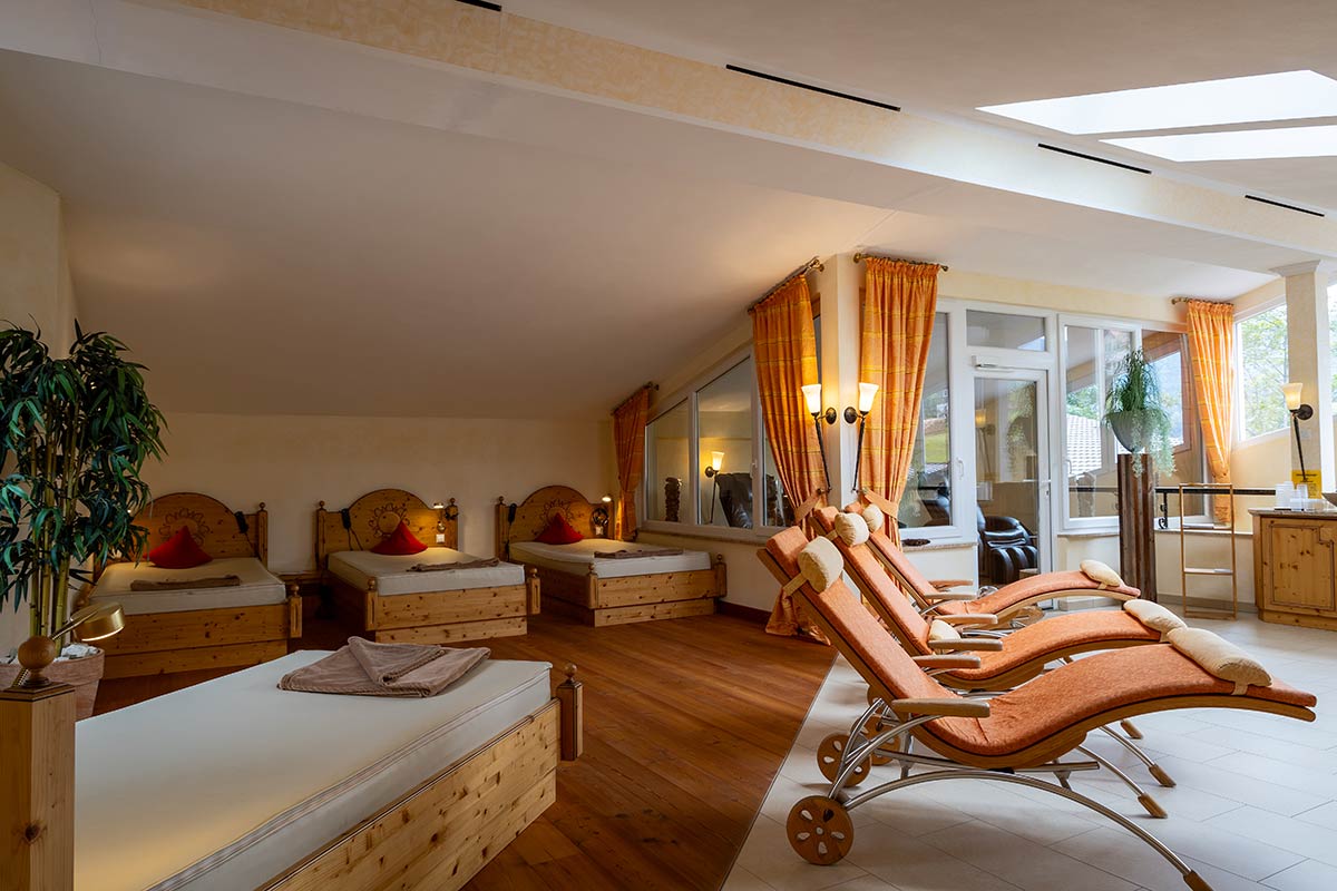 Spa-Zimmer mit Holzliegen, großen Fenstern, orangeroten Decken und gemütlicher Atmosphäre.