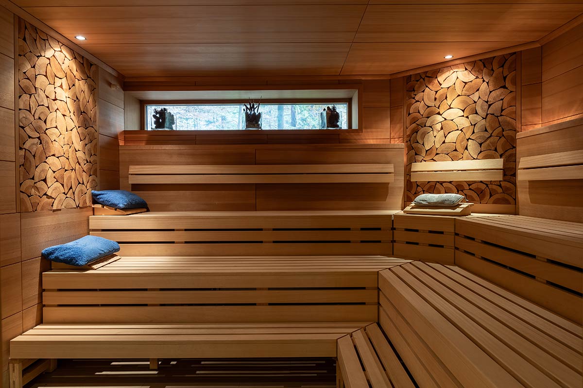 Sauna mit zwei Ebenen Sitzflächen, Wandverkleidung aus hellem Holz und seitlicher Fensteröffnung.