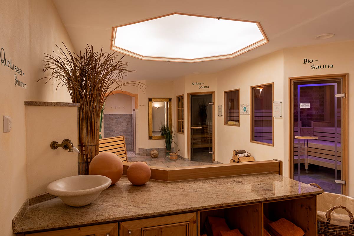 Eingangsbereich Spa mit Sitzgruppe, rustikalen Holzsäulen, Korbmöbeln und sanfter Deckenbeleuchtung.