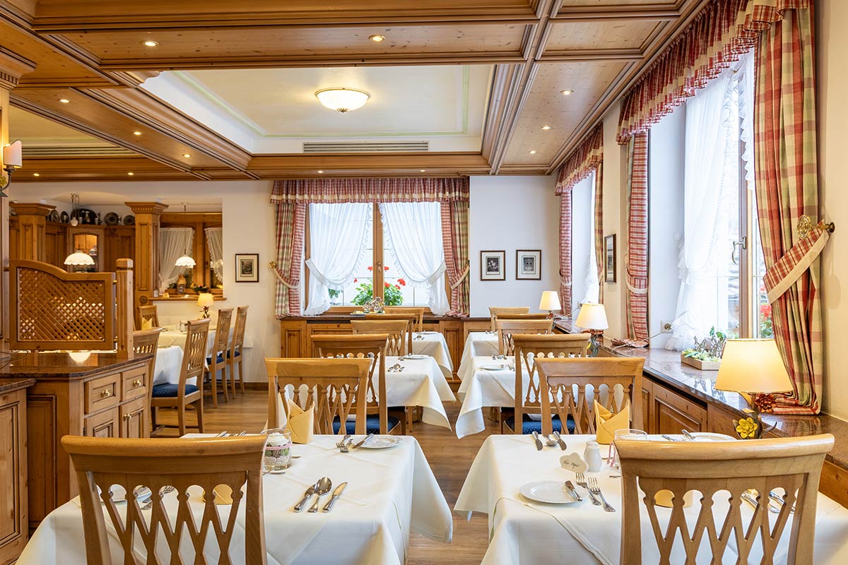 Frühstücksraum mit hellen Holzmöbeln, gedeckten Tischen und Fensterblick nach draußen.