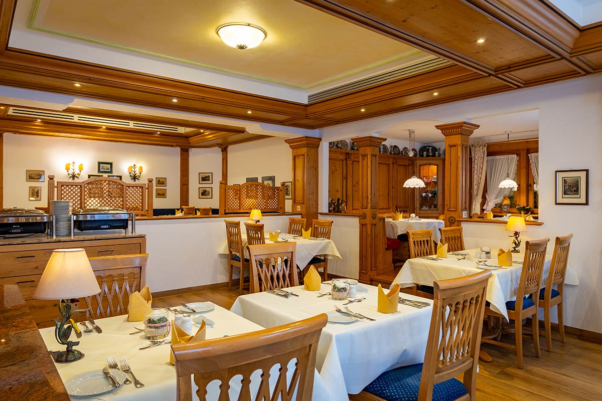 Innenraum mit gedecktem Tisch für vier Personen, Vorhängen, Wandbildern und rustikaler Deckenleuchte.