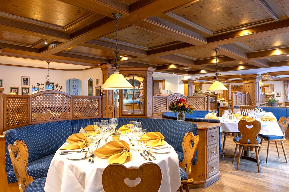 Festlich gedeckter runder Tisch mit Herz-Rückenstühlen, Stoffservietten und Kronleuchter unter dunkler Holzdecke.