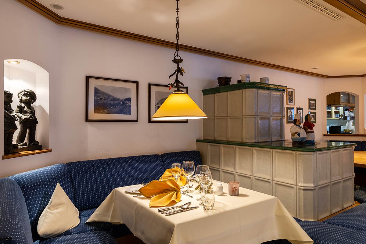 Heller Essbereich mit L-förmiger Polsterbank, zwei gedeckten Tischen, Pendelleuchte und rustikaler Holztäfelung.