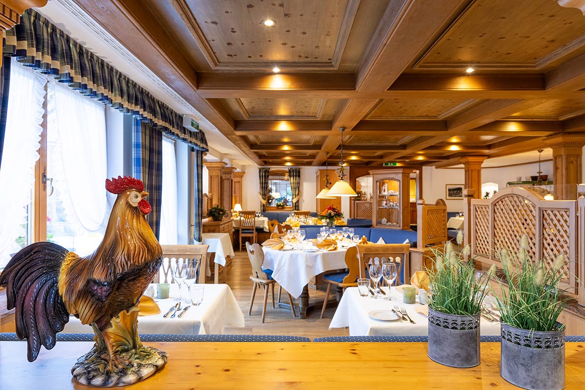 Restaurant mit dunklem Holzboden, Gedecken, Blumenschmuck und offener Fensterfront mit Blick ins Freie.