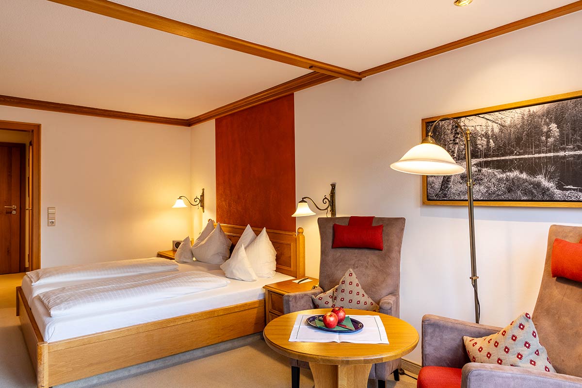 Hotelzimmer mit Doppelbett, dekorativem Kopfteil, rotem Wandakzent und Beistelltisch mit Obstteller.