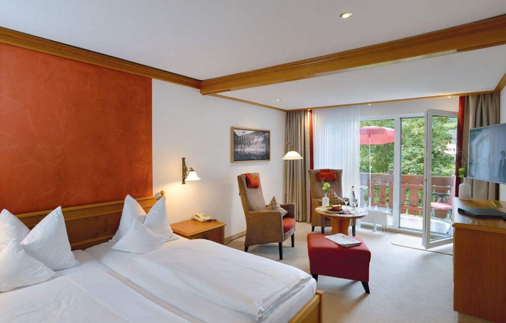 Großzügiges Doppelzimmer Premium mit roter Wandfarbe, Holzmöbeln, Sitzgruppe und Zugang zu Balkon oder Terrasse.