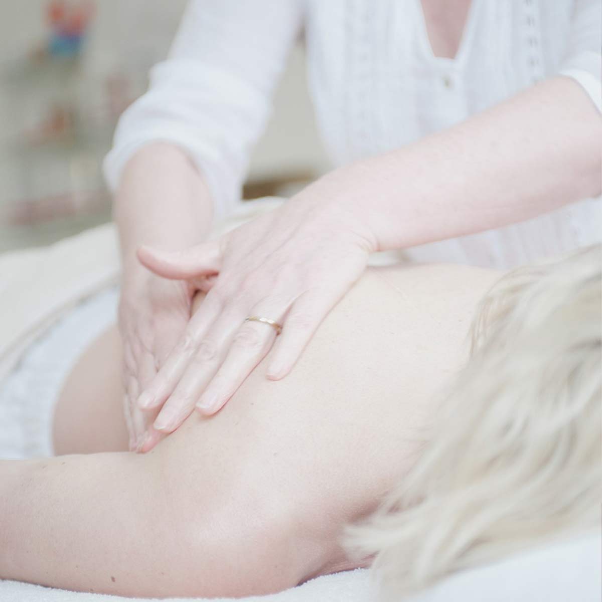 Rückenmassage bei einer blonden Frau, auf dem Bauch liegend.