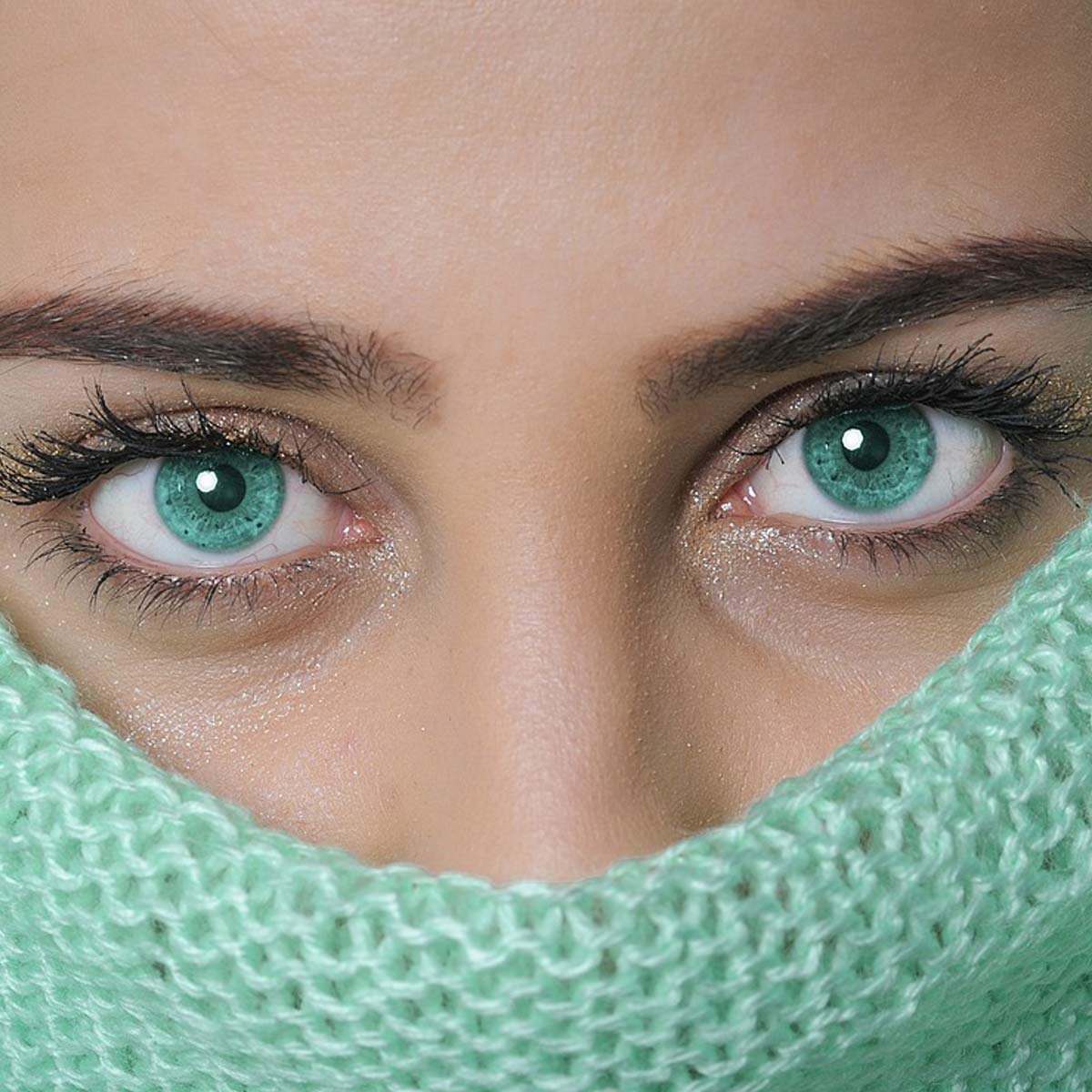 Porträt einer Frau mit grünen Augen, trägt türkisfarbenen Rollkragen, Kopf und Gesicht bis auf die Augen bedeckt, Hintergrund unscharf.