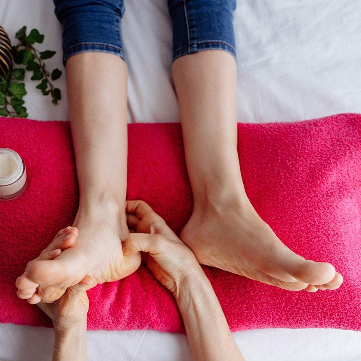 Zwei Paar Füße auf pinkfarbenem Handtuch, daneben Hautpflegeprodukte; Spa-Fußpflege in Vorbereitung.