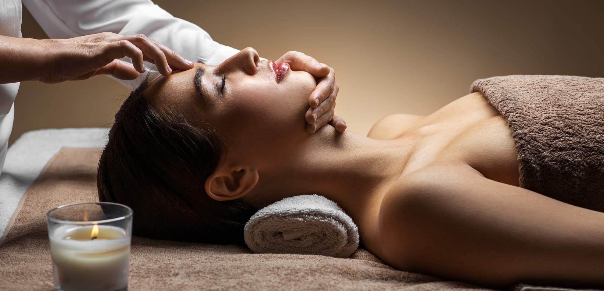 Frau liegt auf Spa-Liege, weißes Nackenkissen unter Kopf, Gesichtsmassage mit seitlichem Druck auf Stirn.