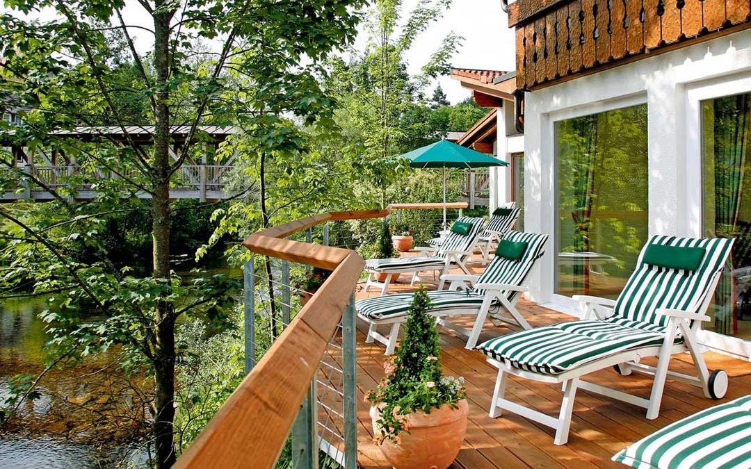 Balkon mit weißer Sitzgruppe und rundem Tisch, Blick auf umliegende Natur, rote Markise leicht eingefahren.